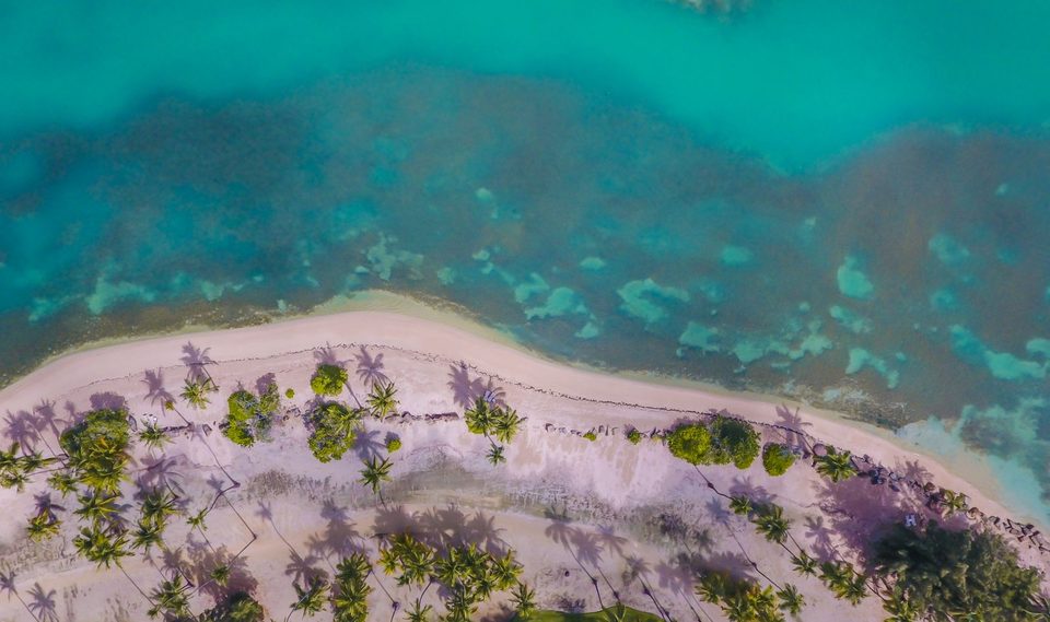 Aerial view of pale sand, palms, and clear water along a Caribbean shore.